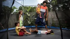 Pai brincando em pula-pula com filhos pequenos