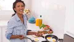 Une femme souriante qui cuit une omelette avec une poêle