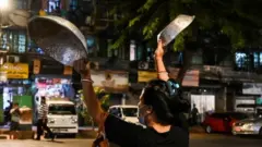 A woman clatters pans to make noise after calls for protest went out on social media in Yangon