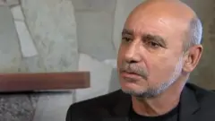 Queiroz aparece sentado dando entrevista