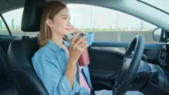 Woman drinking a coffee while sitting behind the wheel of a self-driving car