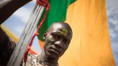 Un homme tient un énorme drapeau national malien lors d'une manifestation de masse à Bamako, le 14 janvier 2022, pour protester contre les sanctions imposées au Mali et à la junte par la CEDEAO