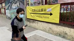 A woman walks past a sign pointing towards a polling station as Hong Kong votes for its legislative council, 19 December 2021
