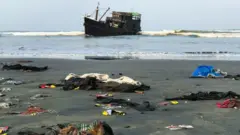 Belongings of Rohingya refugees scattered on the shore as their carrier boat is seen in the background
