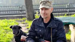 Чоловік із рушницею сидить біля собаки. 