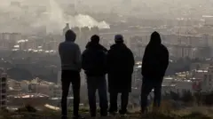 Unos hombres observan cómo se eleva una columna de humo tras una explosión, el 2 de marzo de 2026, en Teherán, Irán. 