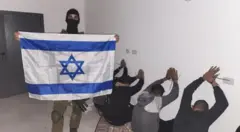 An Israeli soldier posts a photo of detainees while holding an Israeli flag