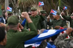Miguel Díaz-Canel, sosteniendo una bandera cubana vestido con uniforme militar, junto a otros oficiales del ejército