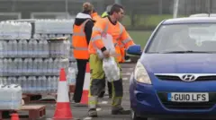 Работники South East Water в яркой спецодежде раздают бутылки с водой водителям