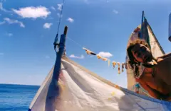 Marco de Candia come un trozo de pescado seco que cuelga de una cuerda sobre la vela de su coche-barco.