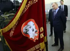 Putin ao lado de bandeiras vermelhas com os rostos de Lenin e Stalin