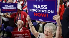 An elderly Trump supporter in a white and red outfit holds a card that reads "Mass Deportation Now".