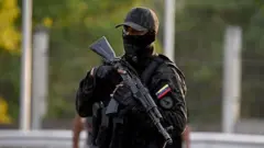 Член Национальной гвардии в камуфляжной форме и с оружием стоит на страже у входа в Форте Тиуна.