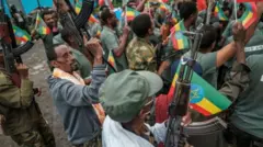 የሚሊሻ አባላት የኢትዮጵያ ባንዲራ እና መሳርያ ይዘው ሲጨፍሩ