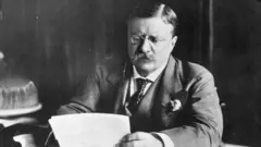 Теодор Рузвельт за рабочим столом с листами бумаги в руках