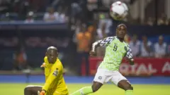 Odion Ighalo wa Nigeria acisha umupira ku munyegori Jonathan Nahimana w'Intamba mu Rugamba