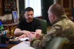 Zelensky sentado na mesa conversando com um general