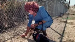 Celia recoge tierra de Cuba a través de la valla de la base de Guantánamo.
