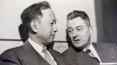 Uma fotografia em preto e branco de Qian Xuesen com seu advogado Grant Cooper em uma audiência de deportação em novembro de 1950