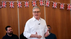 ワイシャツ姿のスターマー氏が立って演説をしている。壁にはたくさんのイギリス国旗が並べてかかっている。周囲には座っている人たちがいる