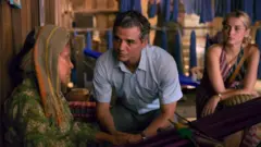 Wagner Moura e Ana de Armas junto com idosa em cena de filme