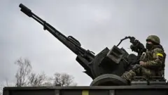 Un soldat ukrainien garde sa position assis sur un canon antiaérien ZU-23-2 sur une ligne de front, au nord-est de Kiev, le 3 mars 2022.