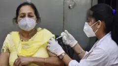 Une femme âgée portant un masque facial se fait vacciner par une femme plus jeune portant un masque facial.