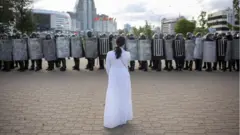 ከአድማ በታኝ ፖሊሶች የቆመች ሴት