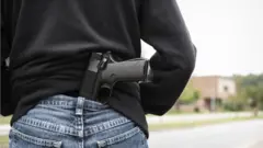 Homem na rua aparece de costas com arma na calça