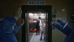 De corredor, equipe de hospital em Wuhan se despede de paciente curado da covid-19, que também acena de dentro de elevador