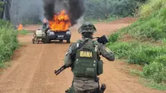 Agente armado de costas, diante de caminhonete em chamas