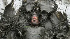 A mud-covered farmer plays in a rice paddy field during National Paddy Day, which marks the start of the annual rice planting season, in Tokha village on the outskirts of Kathmandu, Nepal, on 19 June 2022