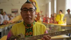Seorang pria memainkan alat musik di dalam kamp.