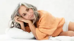 Una mujer mayor acostada sobre una cama. 