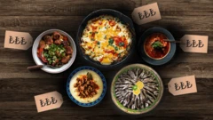 Yemek tarifleri için seçtiğimiz İzmir köfte, hamsili pilav, menemen, beğendili kebap ve tavuk güvecini birer tabak içinde bir masada yan yana getiren bir kolaj. Yemeklerin yanlarında Türk Lirası logoları var