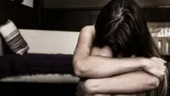 Žena pognute glave rukama obgrljenih oko kolena