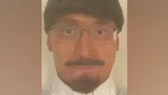 A man wears a fake beard, moustache and wig