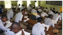 Aworan awọn akẹkọọ ọkunrin ninu yara ikawe, wọn wọsọ funfun ati ṣokoto alawọ erupẹ pupa.