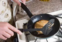Una persona hace una panqueca en una sartén y la voltea con una espátula de plástico.