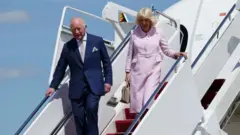 Карл III и Камилла спускаются по трапу самолета