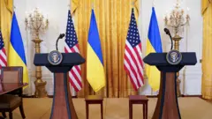 Пустые места перед микрофонами в зале для пресс-конференций на фоне флагов США и Украины