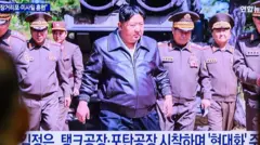 La gente mira una transmisión de 24 horas del canal de noticias Yonhap en una pantalla gigante en la estación de trenes de Seúl, que muestra al líder norcoreano Kim Jong Un inspeccionando un ejercicio de ataque conjunto que involucra sistemas de artillería y misiles de largo alcance de la división del frente oriental del Ejército Popular de Corea, en un lugar no revelado en Corea del Norte.