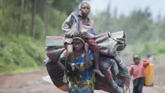 Umugore urimo guhunga imirwano y'inyeshyamba na leta mu myaka ishize, ahetse ibikoresho anatwaye umwana ku rutugu