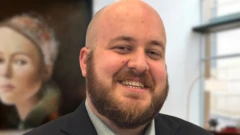 Stephen Jenkins, de terno e camisa azul-marinho, sorrindo