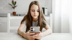 椅子に座りスマートフォンを眺める少女のイメージ写真