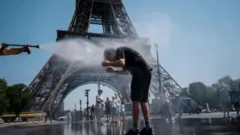 موظف بلدية يرش الماء لتبريد السياح أمام برج إيفل في باريس، في 2 يوليو/تموز 2025، مع موجة حرّ تضرب فرنسا.