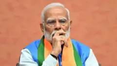 Narendra Modi looks thoughtful sitting at a table covered in flowers