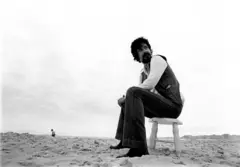 Raul sentado em cadeira na areia da praia