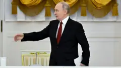 Урочиста зала з білими стінами та великими жовтими драпованими шторами. Ліворуч стоїть прапор Росії, праворуч – прапор із золотим гербом. У центрі кадру – Путін в чорному костюмі з білою сорочкою та червоною краваткою, яка тримає аркуш паперу в лівій руці й робить жест правою рукою.