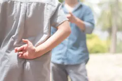 Um menino com os dedos cruzados atrás das costas, enquanto o pai fala com ele